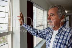 Thoughtful senior man looking through window at nursing home