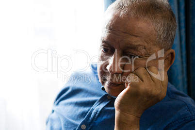 Sad senior man with hand on chin sitting by window