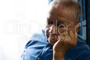 Sad senior man with hand on chin sitting by window