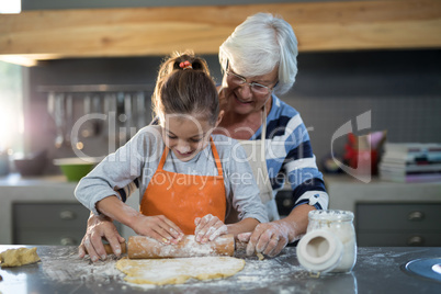 Grandmother helping granddaughter to flatten dough