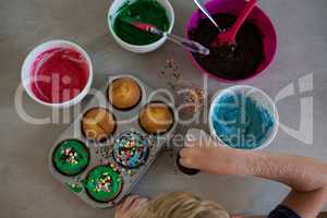 Cropped hand of boy decorating cupcakes with sprinklers
