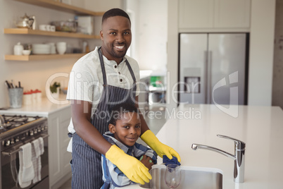 Smiling father and son cleaning wine glass in kitchen