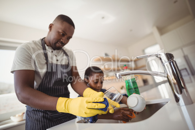 Father and son cleaning utensils in kitchen