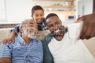 Smiling multi-generation family taking selfie from mobile phone in living room