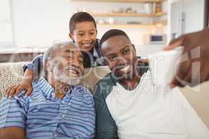 Smiling multi-generation family taking selfie from mobile phone in living room