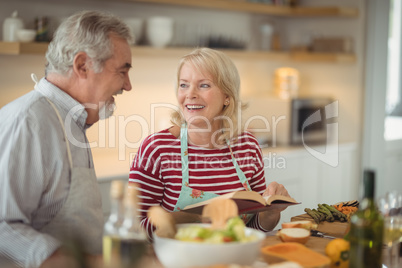 Senior couple reading recipe book while preparing meal