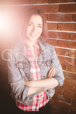 Smiling woman standing with arms crossed against brick wall