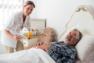 Portrait of female doctor serving food to senior patient relaxing on bed