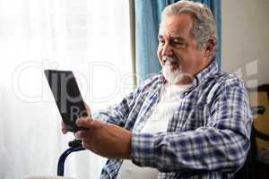 Smiling senior man using digital tablet by sitting on wheelchair