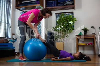 Female physiotherapist helping girl patient in performing stretching  exercise on exercise mat