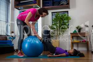 Female physiotherapist helping girl patient in performing stretching  exercise on exercise mat
