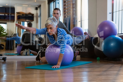 Physiotherapist assisting senior woman in performing exercise on fitness ball