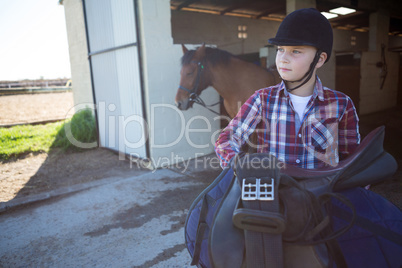 Teenage girl holding horse equipments in the stable