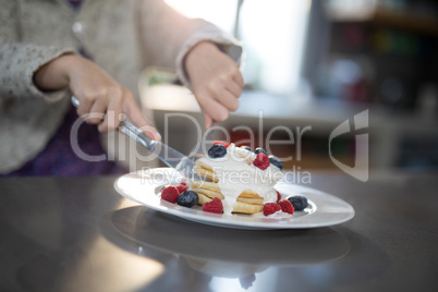 Little girl cutting a fruit pancake with a fork and knife