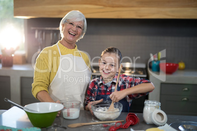 Granddaughter mixing flour in a bowl while posing with grandmother