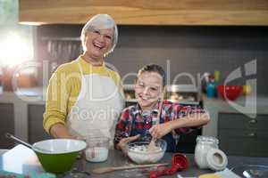 Granddaughter mixing flour in a bowl while posing with grandmother