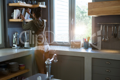Woman adjusting books on shelf in kitchen