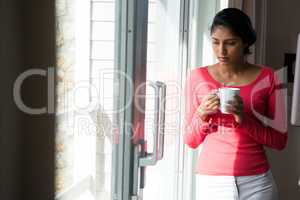 Thoughtful woman with coffee cup by window