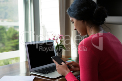 Young woman with laptop using phone