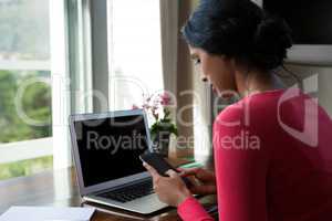 Young woman with laptop using phone