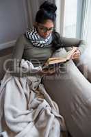 Young woman reading book by window on sofa