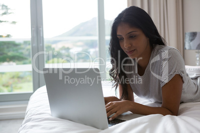 Woman using laptop while resting on bed