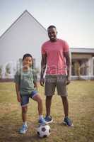 Smiling father and son standing in garden with football