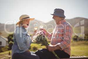 Senior man offering a flower bouquet to senior woman while having white wine