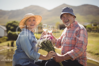 Senior man offering a flower bouquet to senior woman while having white wine