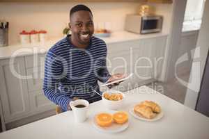 Smiling man using a digital tablet while having breakfast in kitchen