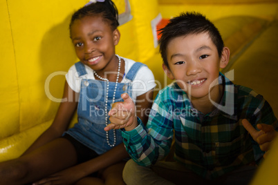 Portrait of girl and boy sitting on bouncy castle