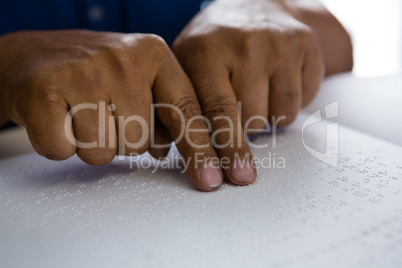 Cropped fingers on senior man reading braille book at table