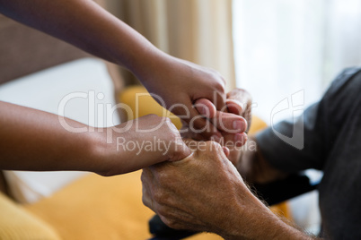 Female doctor and senior man holding hands in nursing home