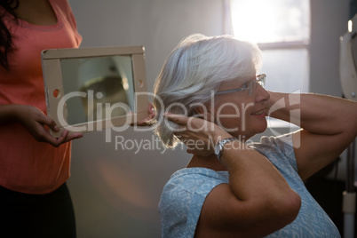 Midsection of hairstylist showing hair in mirror to senior woman