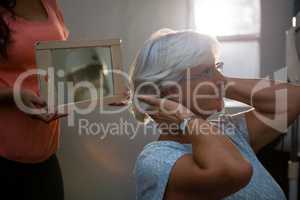 Midsection of hairstylist showing hair in mirror to senior woman