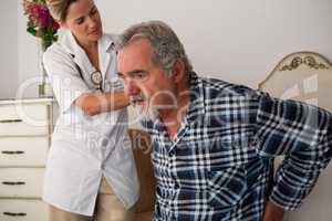 Female doctor assisting senior patient in sitting on bed