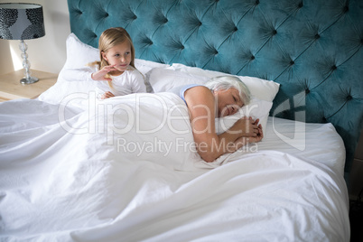 Grandmother sleeping on bed while girl sitting behind her