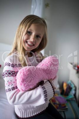 Smiling girl holding heart shape pillow on bed