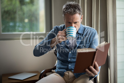 Man reading book while having coffee in living room