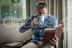 Man reading book while having coffee in living room