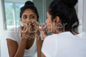 Woman squeezing pimple reflecting on mirror