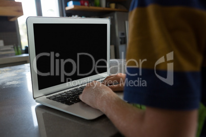 Cropped hands of boy using laptop in kitchen