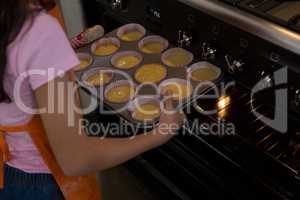 Girl keeping muffin tin in oven at kitchen