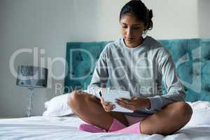 Full length of woman using digital tablet on bed