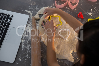 Cropped image of girl making shape on dough in kitchen