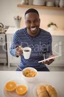 Smiling man using a digital tablet while having cup of coffee in kitchen