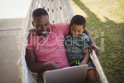 Father and son using laptop while relaxing on hammock