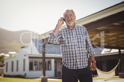 Senior man talking on mobile phone outside his house