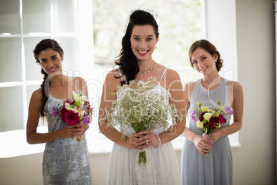 Bride and bridesmaids standing with bouquet at home