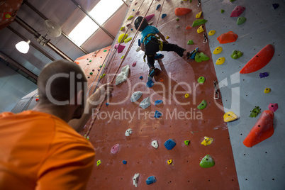 Trainer assisting boy in rock climbing